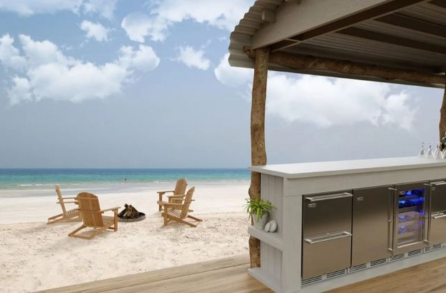 front view of the beach from behind an outdoor tiki bar with stainless steel outdoor refrigerators behind the bat