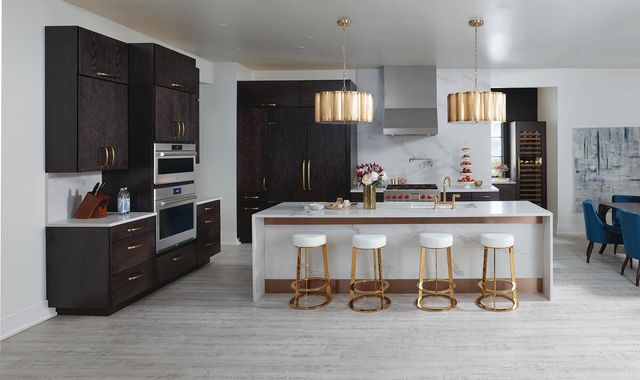 Front view of a modern kitchen with white walls, dark brown cabinetry, a white marble island, and a Wolf E series double wall oven