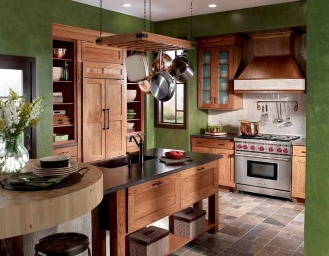 front view of a boho kitchen with green limewash walls, light wooden cabinetry, and a stainless steel Wolf range