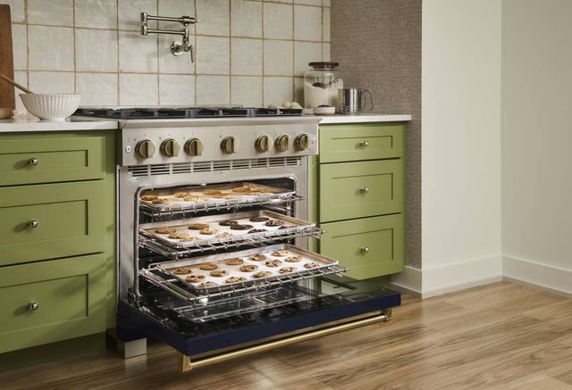 Front view of a modern kitchen with an opened BlueStar range with three pans of cookies baking inside