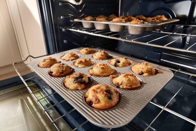 Front view of an opened Whirlpool oven with two pans of muffins cooking inside