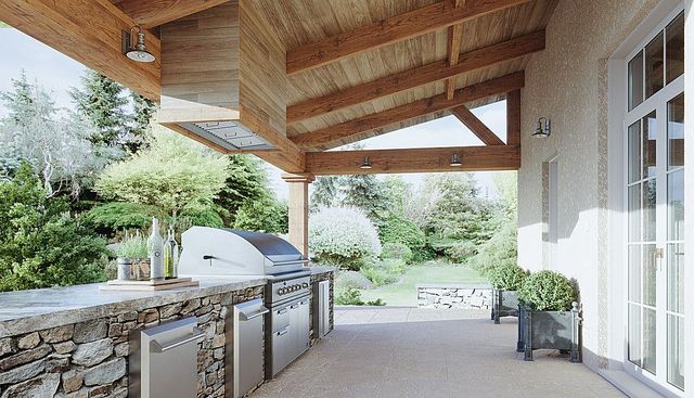 View of an outdoor kitchen with a grill and range hood in a lush backyard