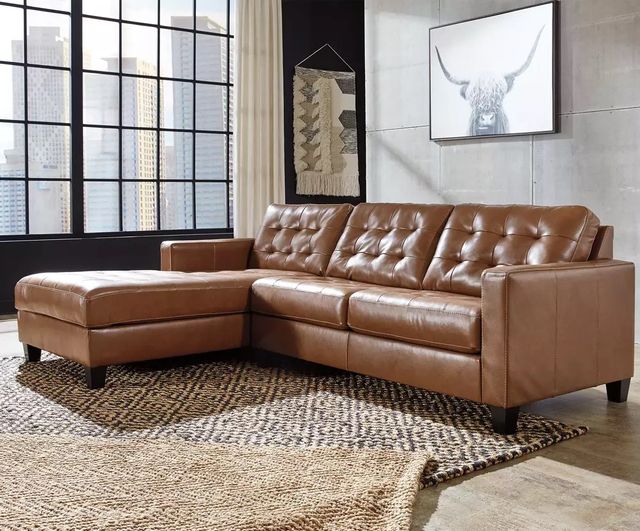front right angled view of  a brown leather chaise sofa in a rustic living room with large windows