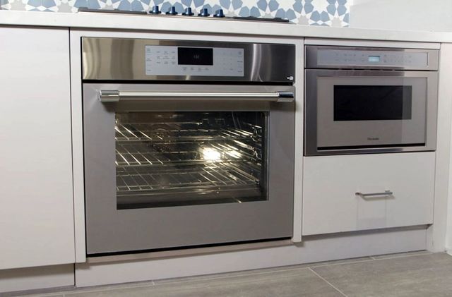 front view of a thermador electric wall oven and microwave built into white cabinetry under a counter