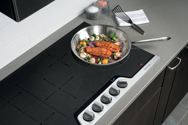Front view of a modern 36 inch induction cooktop with stir fry cooking on top.