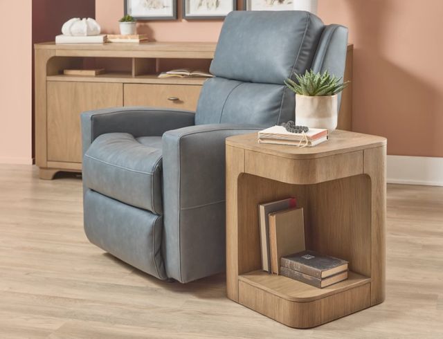 Front view of a light wooden sculptural end table next to a recliner
