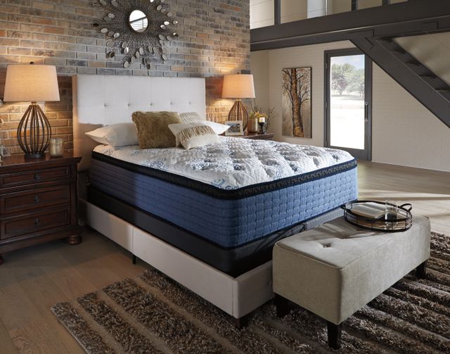 front view of a rustic bedroom with a full size mattress on a modern frame against a brick wall. The bed has pillows on top and there are side tables on both sides.