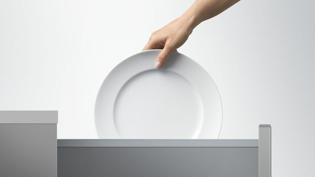 View of a hand reaching into frame to pull a clean plate out of a Fisher and Paykel dishdrawer.
