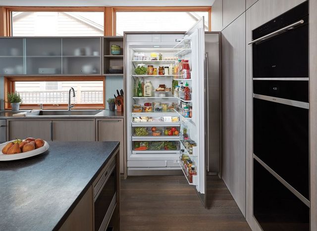 Front view of a modern luxurious kitchen with an opened Sub-Zero column refrigerator, fully stocked. 