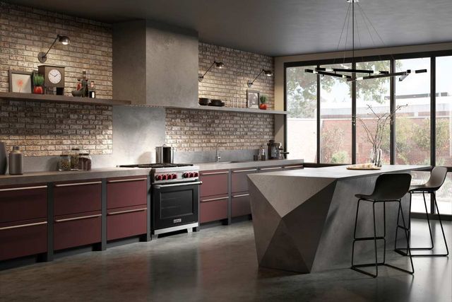 view of a modern kitchen with a beige brick wall, burgundy cabinetry, and a black Wolf gas range 