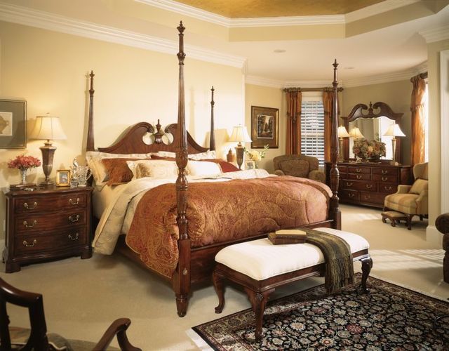 front view of a traditional bedroom with a wooden ornate poster bed and matching nightstands and dresser