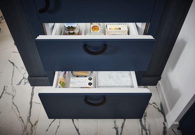 Close view of a Sub-Zero bottom freezer refrigerator with the bottom drawers pulled out to show the ice reservoir and frozen goods.
