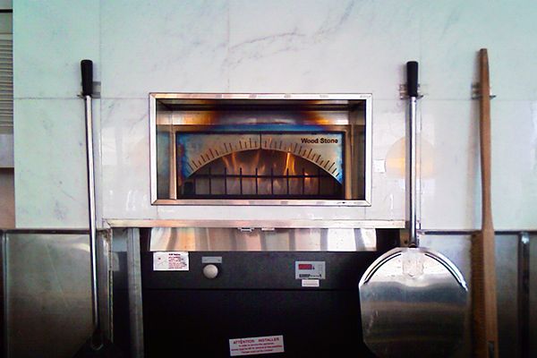 Front view of a Wood Stone pizza oven built into a modern kitchen with a white marble exterior.