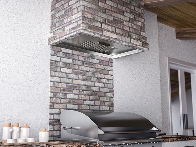 View of an outdoor kitchen with a built in grill and vent hood.
