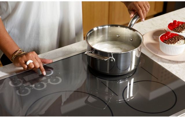 View of a person cooking on a 36" induction cooktop and using the touch controls.