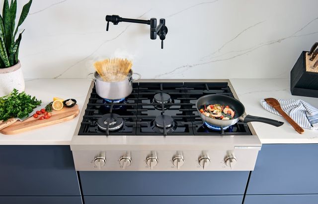 Front view of a Bosch rangetop with pasta and shrimp cooking in pans on top.