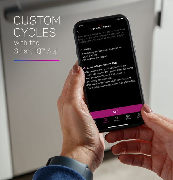 A person using a smartphone to control a GE Profile smart dishwasher in a bright kitchen.