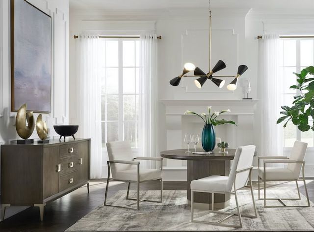 front view of a modern dining room with a wooden accent cabinet, white walls, and brass accents
