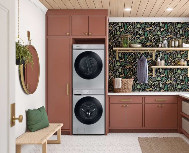 front view of a modern laundry room with pink cabinetry, green floral wallpaper, and a silver stackable washer and dryer