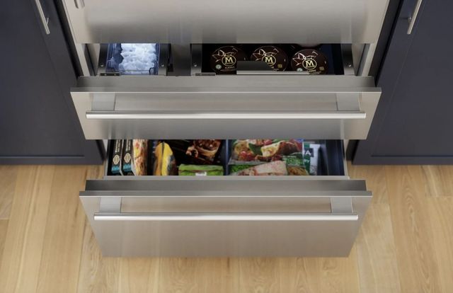 Close view of a Thermador bottom freezer refrigerator with the bottom freezer drawers pulled out showing frozen good and the ice reservoir. 