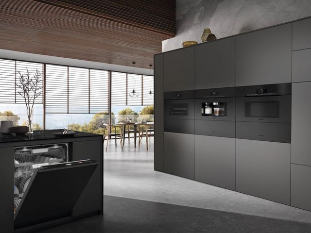Front view of a contemporary kitchen with matte black Miele appliances including a wall oven, coffee machine, and dishwasher
