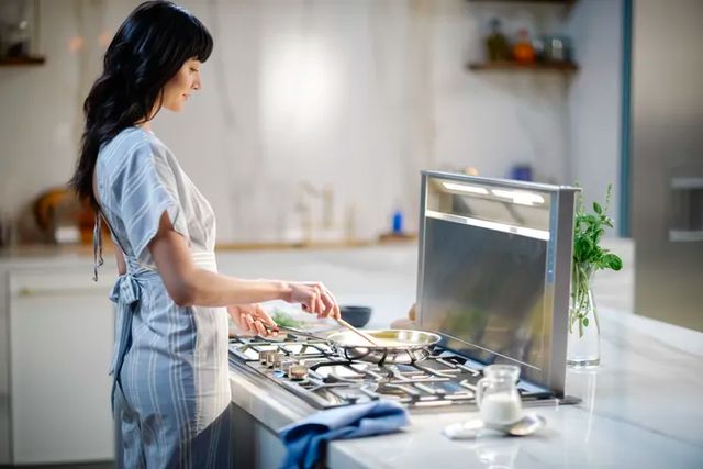 Side view of a woman cooking on a Thermador cooktop with a downdraft range hood