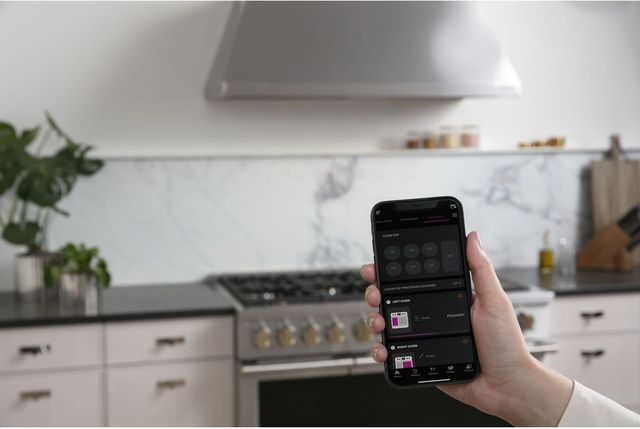 Front view of a person holding a phone up showing the SmartHQ app in front of a Monogram range in a modern kitchen.