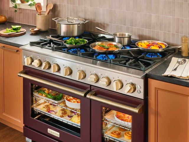 Front view of a luxury kitchen with a BlueStar dual fuel range with dinner being cooked isnide and on top