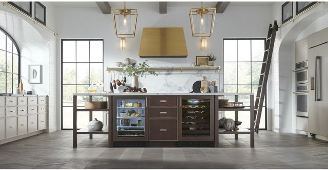 Front view of a gold Monogram range hood in a modern white kitchen