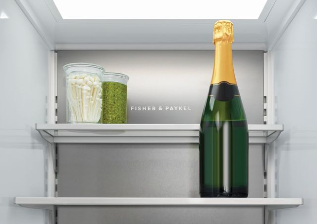 Front view of the inside of a Fisher & Paykel refrigerator with a wine bottle, jars of veggies, and the Fisher & Paykel logo on the back