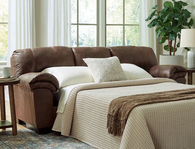 View of a leather sofa bed pulled out and set up in a modern living room with large windows behind it.