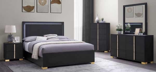 View of a modern bedroom with a sleek black bedroom set with gold accents and white walls.