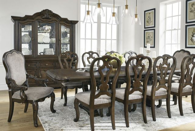 front view of a traditional dining room with white walls and dark ornate wooden dining furniture including a table, 10 seats, and a dining hutch
