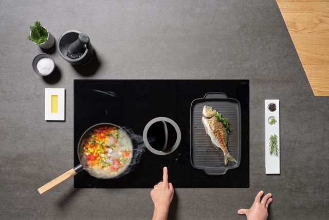 Credit: Elicia Front view of an Elica downdraft cooktop with a person's hand pointing at the downdraft system