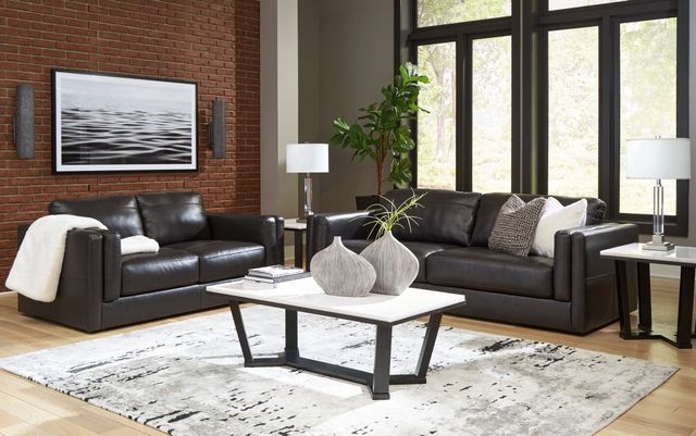 front view of a black leather sofa in a contemporary living room with grey accents and brick walls