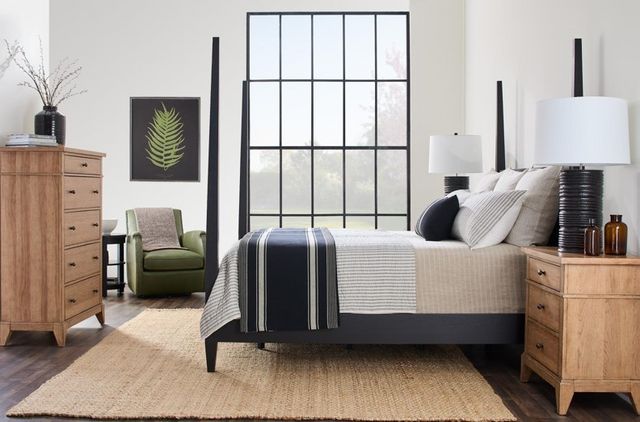 Side view of a casual bedroom with a black four poster bed and light wooden nightstands and dresser