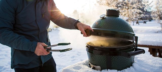 View of a man opening a Big Green Egg outside in snow