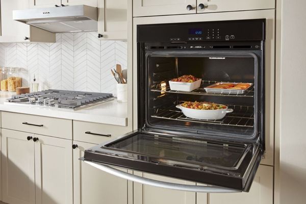A person taking a dish out of an eye-level wall oven