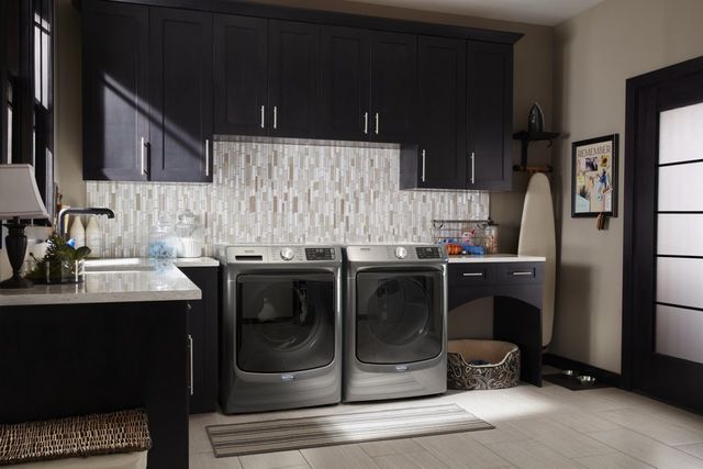 front view of a modern laundry room with dark grey laundry appliances and black cabinetry